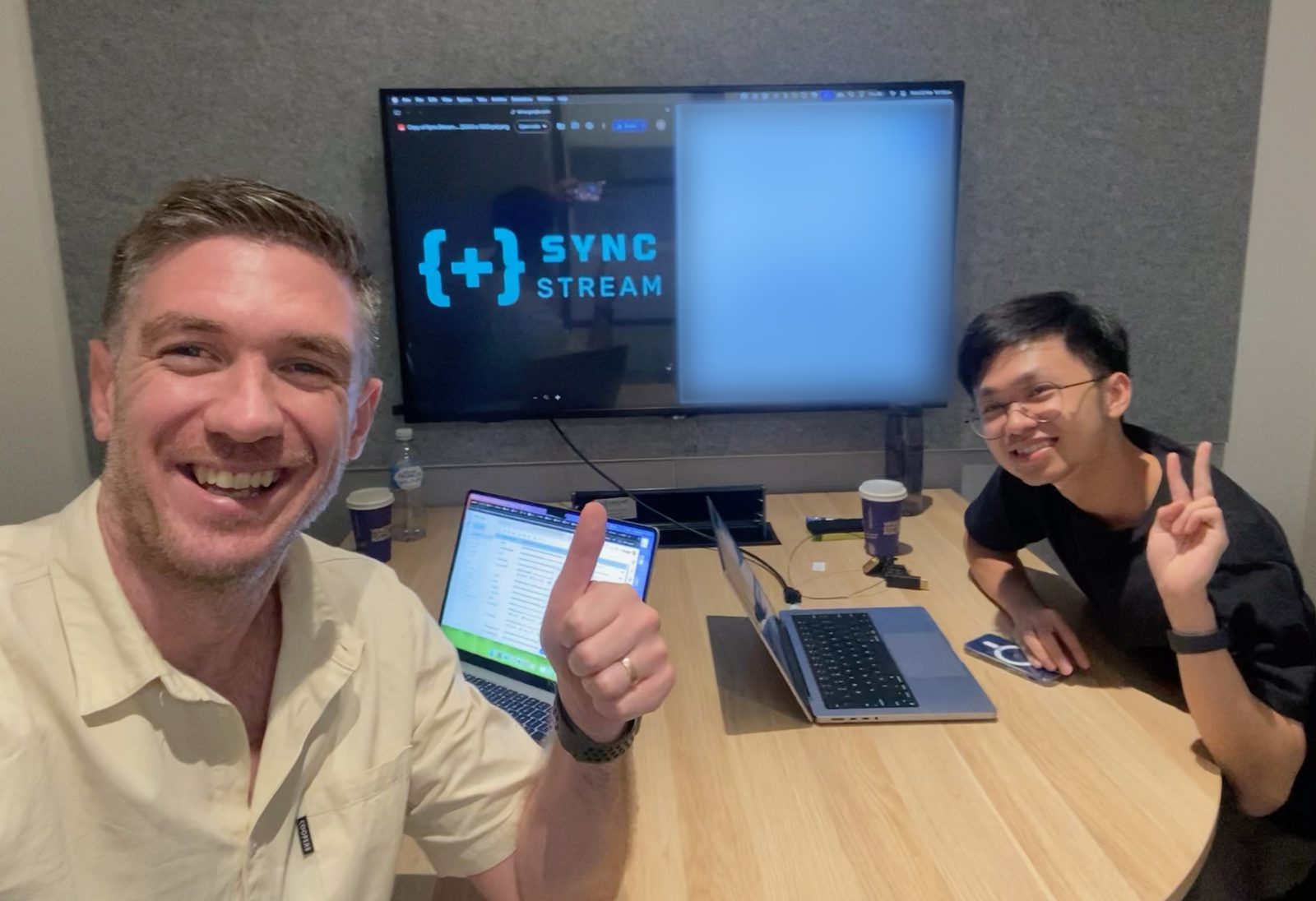 Ben and Quan in a meeting room, with the Sync Stream logo on the screen behind them
